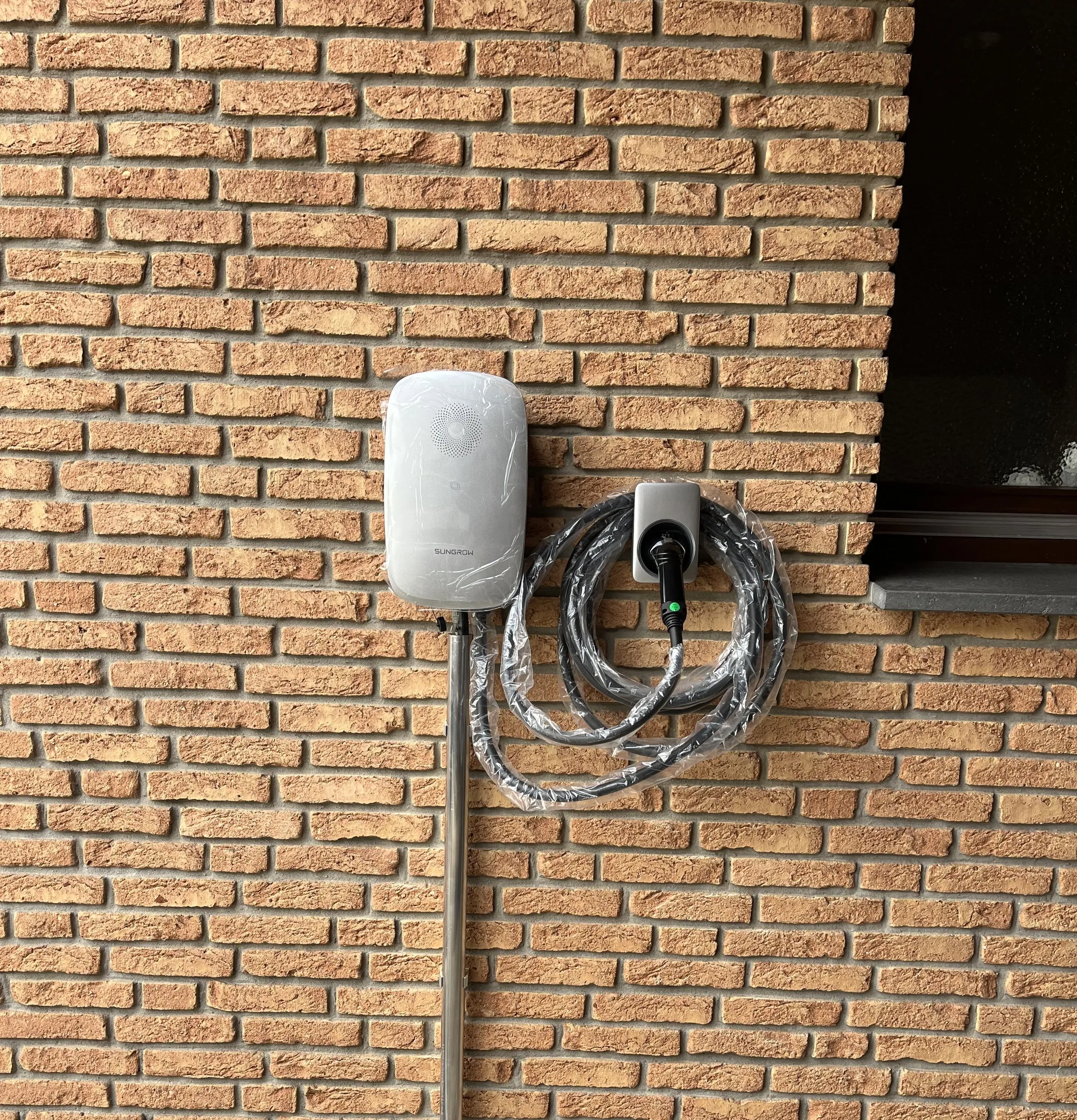 Wallbox mit Ladekabel an einer roten Klinkerwand